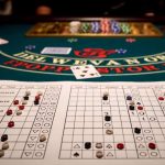Fekvő blackjack alapstratégia tábla színes zsetonokkal megjelölve egy igazi kaszinó zöld posztós blackjack-asztalán, kártyákkal és zsetonokkal a háttérben.